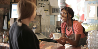 Awoman handing another woman a cup of coffee at a counter