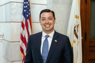 Treasurer James A. Diossa stands in front of the American and Rhode Island flags.